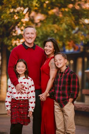 A family wearing coordinated red and white outfits poses together for holiday photos in an autumn outdoor setting.