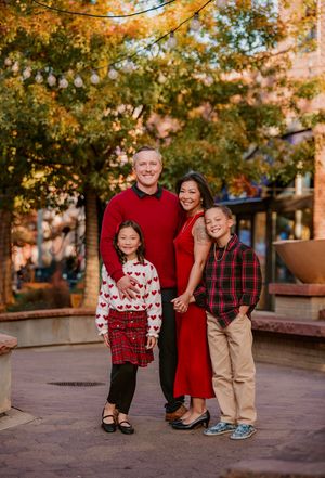 Family wearing coordinated red and plaid outfits poses together during autumn photo session on brick walkway.