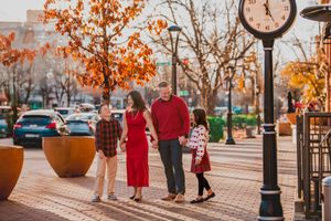 A family walks along a brick-paved path during autumn with orange trees and lamp posts lining the street.