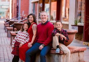 Family wearing coordinated red and navy outfits poses together for outdoor holiday photos on brick steps.