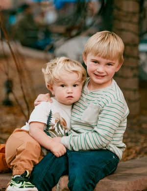 Two young children in casual clothing sit together on wooden steps in an outdoor setting.