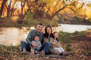 A group enjoys a playful autumn moment together on fallen leaves by a lake during golden hour sunset.