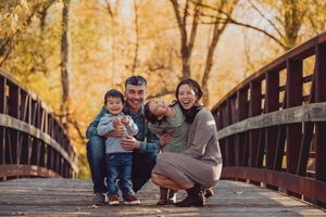 A family enjoys a playful autumn moment together on a wooden bridge surrounded by golden fall foliage.