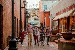 People walk through a covered brick walkway with storefronts and hanging plants creating an urban shopping atmosphere.