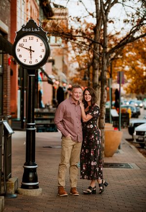 A couple shares a romantic moment on a brick sidewalk during autumn with vintage street lamps and fall foliage.
