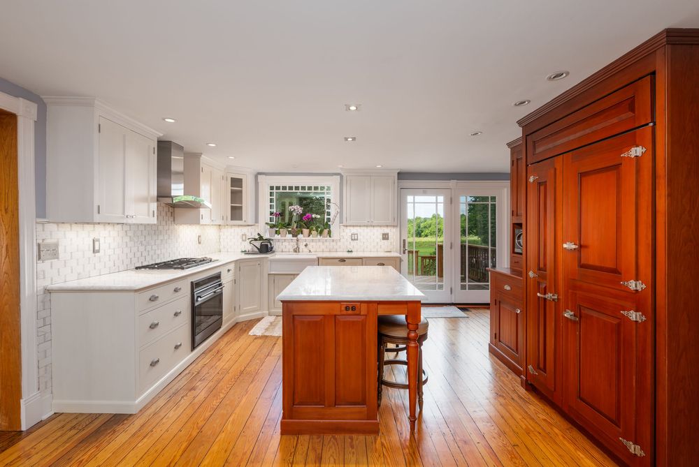 Modern kitchen interior with contrasting white cabinets and rich cherry wood accents featuring hardwood floors and stainless appliances.