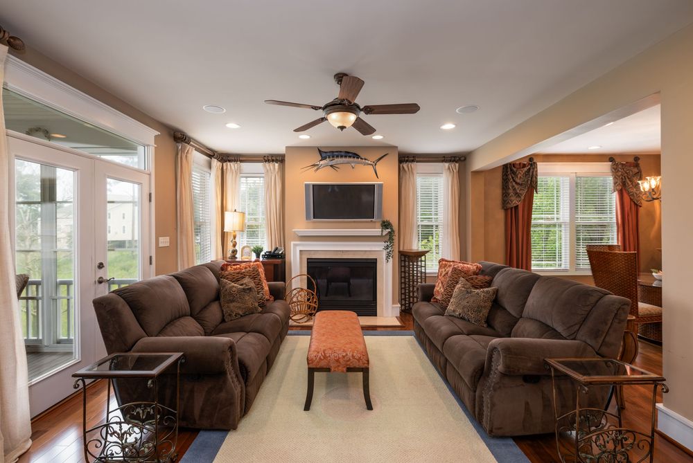 Cozy living room with brown sectional sofas, fireplace, mounted TV, and ceiling fan in warm neutral tones.