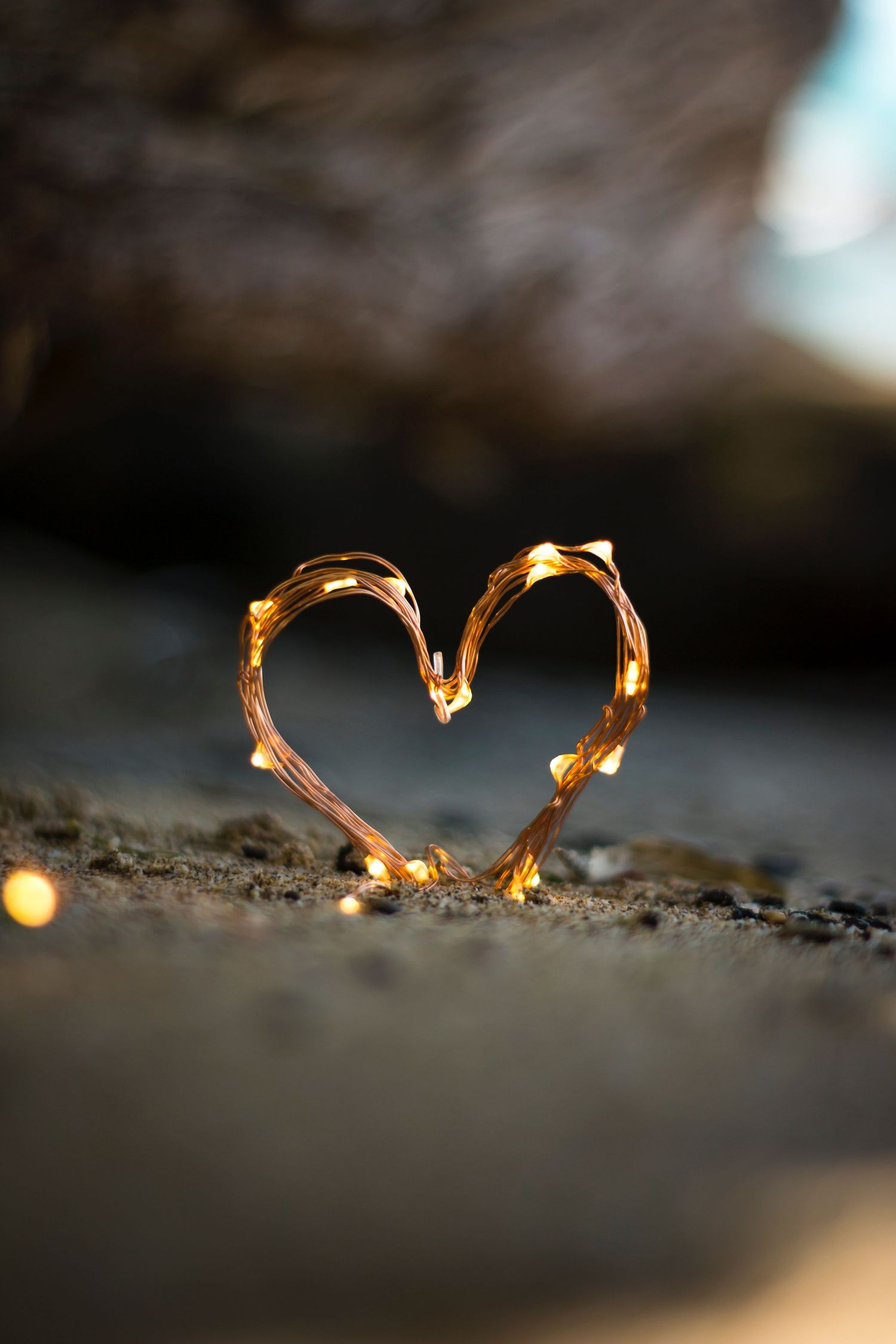 Delicate string lights arranged in a heart shape glowing warmly against a dark textured surface.