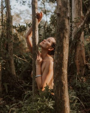 A person in a forest gazes upward at the sunlight filtering through tree branches in a dreamy outdoor scene.