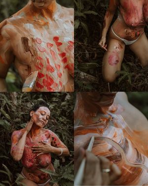 Artistic body painting session in a natural outdoor setting featuring red heart designs and white paint details.