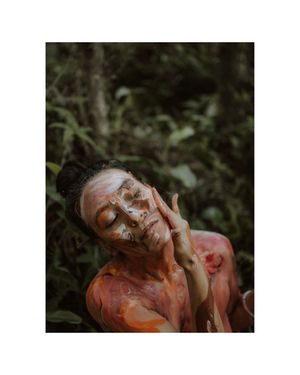 Artistic portrait with orange and white body paint against dark foliage background.