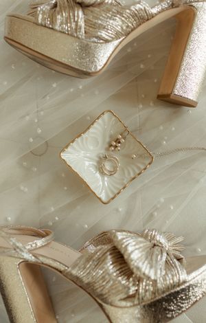Gold wedding shoes and accessories arranged on white tulle fabric.
