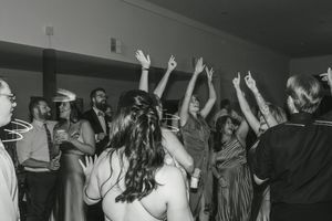 Wedding reception guests dancing with hands raised on a dimly lit dance floor.