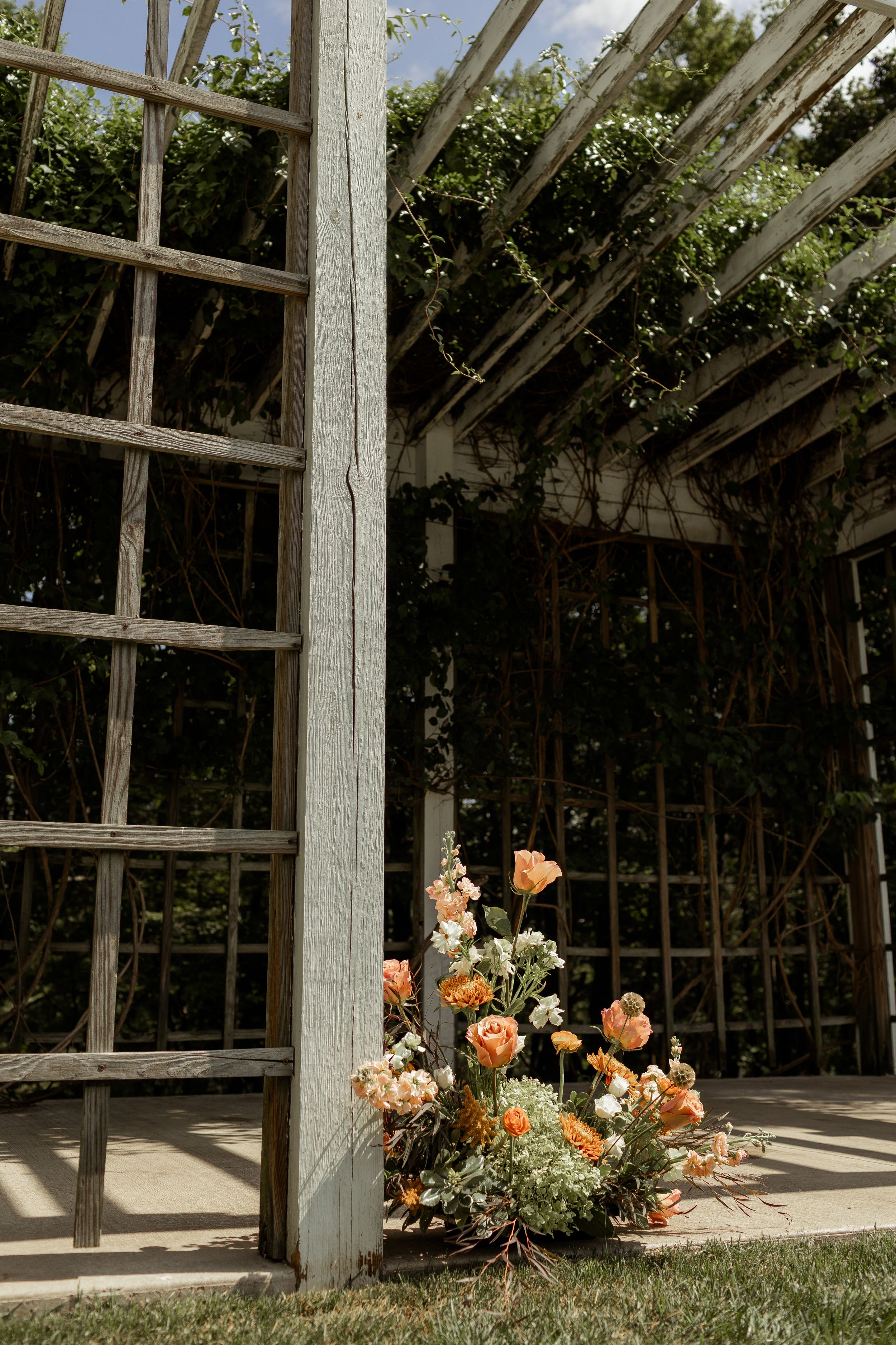 Rustic greenhouse interior with natural light streaming through windows and orange floral arrangements on the ground.