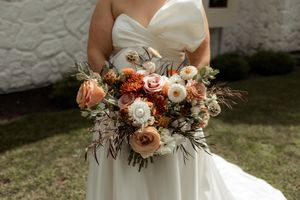 A romantic bridal bouquet featuring blush roses, white ranunculus, and dried foliage in a natural garden style arrangement.