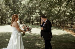 A couple shares their first look in a wooded outdoor setting.