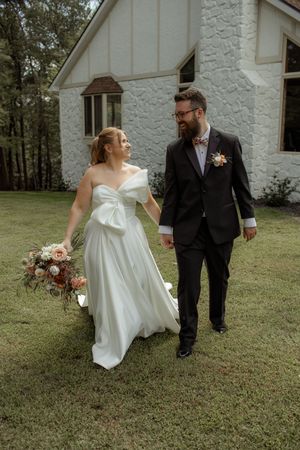 Wedding couple walking and laughing together outside a white church building.