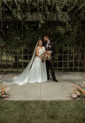 Wedding couple poses together on a garden path with lush greenery and decorative flowers.