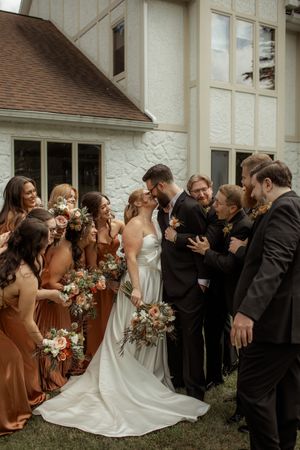 Wedding celebration outside white church building with attendees in formal attire and rust-colored bridesmaid dresses.
