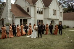 Wedding party lined up outside white church buildings for formal group photo.