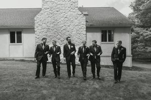 Vintage black and white photo of groomsmen posing outside a white stone building.