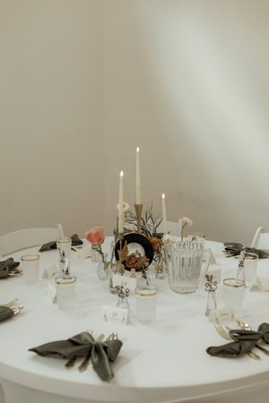 Elegant white wedding reception table setting with candles and minimalist decor against neutral background.