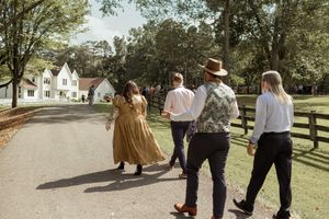 A group walks together on a sunny day along a rustic wooden fence at a countryside venue.