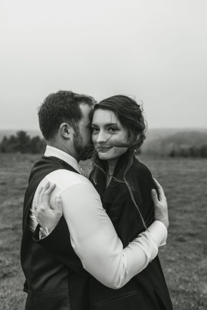 Intimate black and white portrait of a couple embracing in a field.