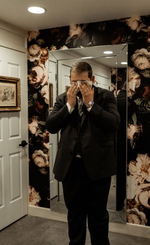 Emotional moment of wedding preparation in room with floral wallpaper.