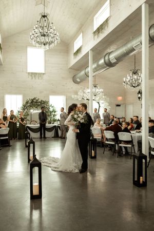 Newlyweds share first dance in elegant venue with chandeliers and lantern-lined aisle.