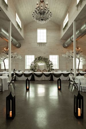 An elegant wedding venue with a floral arch, chandeliers, and lantern-lined aisle.