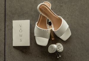 White bridal shoes and wedding vows displayed with elegant jewelry on dark surface.