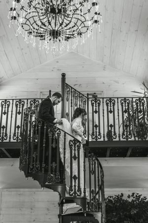 An ornate spiral staircase with a crystal chandelier in a rustic white venue.