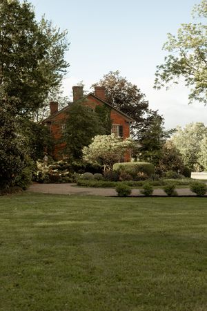 A scenic view of a historic brick house set on a sprawling green lawn with mature trees.