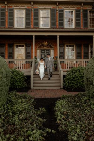 Historic Victorian house exterior with wide porch, brick path, and ornate architectural details surrounded by lush greenery.