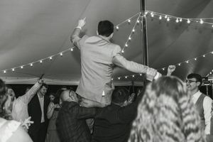 Wedding guests dancing together under white string lights in a large tent during evening reception festivities.