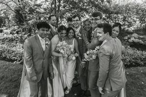 Wedding party members laugh together outdoors during casual candid photo moment in garden setting.