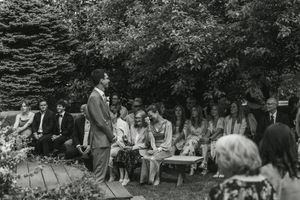 Vintage black and white photograph of outdoor gathering in a garden with audience seated on benches surrounded by trees.