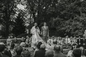 Vintage black and white photo showing an outdoor wedding ceremony with guests seated in a wooded setting.