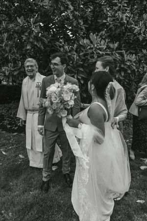 Wedding party gathered outdoors in front of lush green foliage during a summer ceremony.