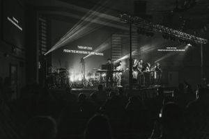 Concert stage illuminated with dramatic lighting and text projections in black and white.