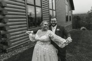 A joyful couple celebrates their wedding day in front of a log cabin-style building.