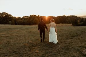 Couple walking hand in hand through a field at sunset after their wedding ceremony.