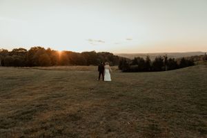 Distant shot of newlyweds standing in an open field during golden hour.