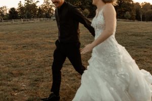 Couple walking through a rustic field during golden hour in wedding attire.
