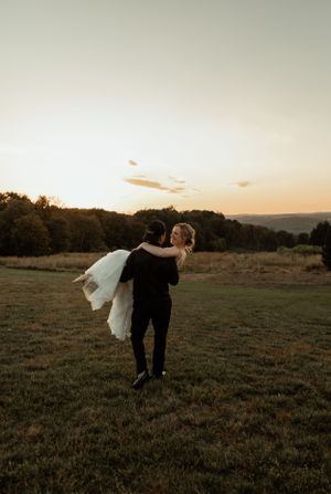 Romantic sunset moment as groom carries bride in an open field.
