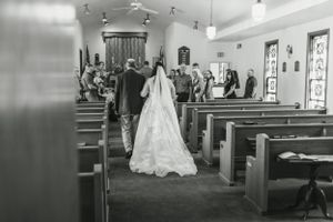A black and white photo of a church wedding ceremony in progress viewed from the back.