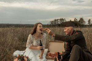 Playful couple enjoys pizza picnic in field during sunset photo session.