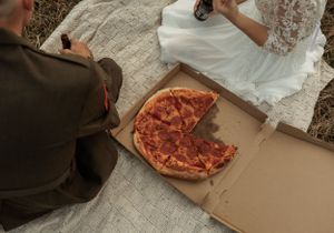 Close-up of couple sharing pizza during outdoor wedding photoshoot.