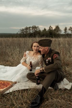 Romantic couple enjoying drinks and pizza during rustic outdoor celebration.